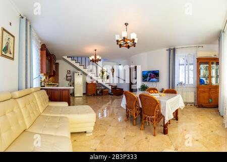 Grande salle lumineuse Sunny dans la maison. Au centre de la chambre se trouve une table avec une nappe blanche et quatre chaises en osier. Canapé en cuir blanc. Vintage Banque D'Images