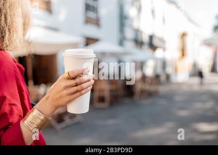 Femme tenant une tasse de papier avec du café pour aller sur l'arrière-plan de la rue de la vieille ville, gros plan sur la main avec le café Banque D'Images