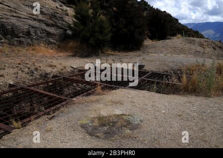 Une grille en acier et en fil métallique bloque un puits de mine dans l'ancienne zone d'extraction d'or de la réserve historique de Bendigo, Central Otago, Nouvelle-Zélande. Banque D'Images