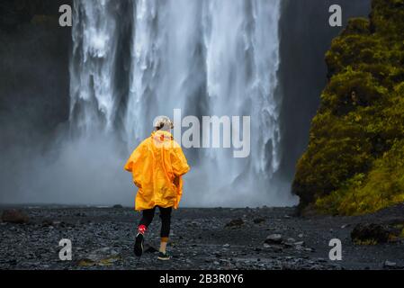 Les touristes portent un imperméable jaune qui se promène à la cascade de Skogafoss en Islande Banque D'Images