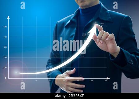Homme d'affaires qui dessine une courbe exponentielle d'un progrès dans les performances de croissance des affaires, retour sur investissement - ROI, sur un écran virtuel de présentation. Banque D'Images