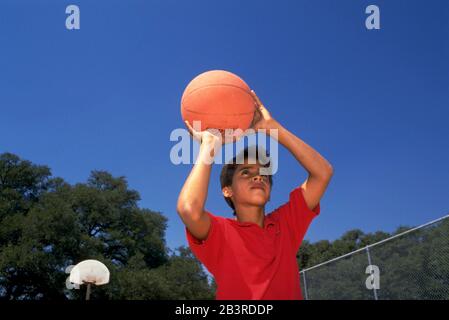 Austin Texas États-Unis, vers 1988 : un adolescent hispanique pratique le tir d'un basket-ball dans un terrain de basket-ball de parc de quartier.©Bob Daemmrich Banque D'Images