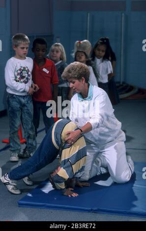 Austin Texas USA: Un professeur de gym aide l'élève à faire un somersault sur un tapis de ventre pendant la classe d'éducation physique dans le gymnase de l'école élémentaire.©Bob Daemmrich Banque D'Images