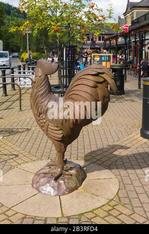 Magasins de vente au détail cafés et sculpture sur coq en fonte à l'extérieur de la gare de Betws y-Coed dans le parc national de Snowdonia au nord du Pays de Galles Banque D'Images