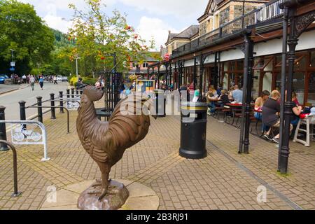 Magasins de vente au détail cafés et sculpture sur coq en fonte à l'extérieur de la gare de Betws y-Coed dans le parc national de Snowdonia au nord du Pays de Galles Banque D'Images