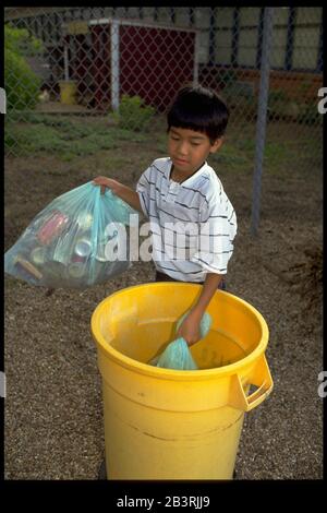 Austin Texas USA: Un garçon coréen-américain met des sacs remplis de déchets qu'il a ramassés sur le terrain de l'école dans une poubelle en plastique.©Bob Daemmrich Banque D'Images