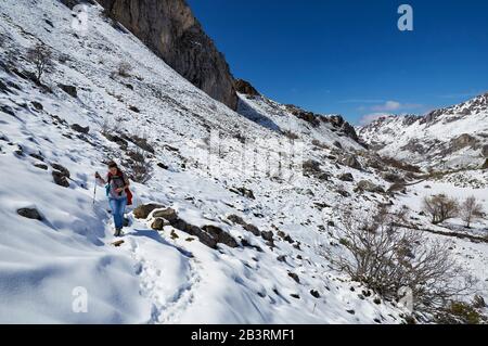 Randonneur féminin dans la piste de randonnée PR.AS-15.1 recouverte de neige avec des montagnes escarpées au loin (Valle del Lago, Soriedo Natural Park, Asturies, Espagne) Banque D'Images