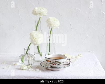 Cadre élégant avec des fleurs de ranunculus blanches et une tasse de thé Banque D'Images