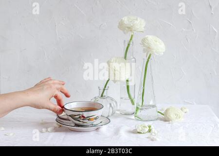 Table avec fleurs blanches et main de femme tenant une tasse de thé Banque D'Images