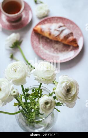 Fleurs de ranunculus blanches et une tasse de thé avec croissant flou à l'arrière-plan Banque D'Images