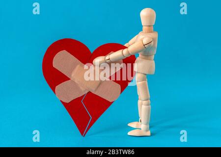 Mauvaises relations, rupture, tristesse émotions concept. Homme en bois tenant le coeur brisé fixé avec un bandage en plâtre. Banque D'Images