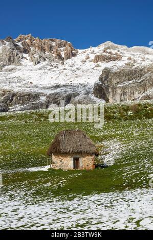 Teito, une demeure traditionnelle en pierre avec toit de chaume, avec des montagnes escarpées en arrière-plan (Valle del Lago, Soriedo Natural Park, Asturies, Espagne) Banque D'Images