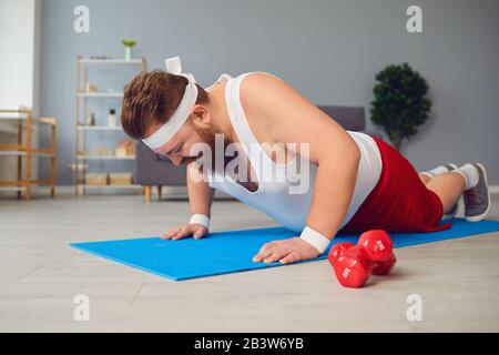 Drôle de gros homme faisant des exercices sur le sol souriant sur le sol à la maison. Banque D'Images