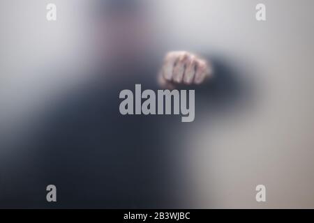 Poing mâle derrière la paroi en verre mat, photo abstraite Banque D'Images