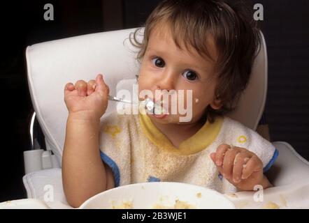 Austin Texas USA, 1995: Bébé garçon de 17 mois aime manger avec une cuillère tout en étant assis dans une chaise haute. M. ©Bob Daemmrich Banque D'Images