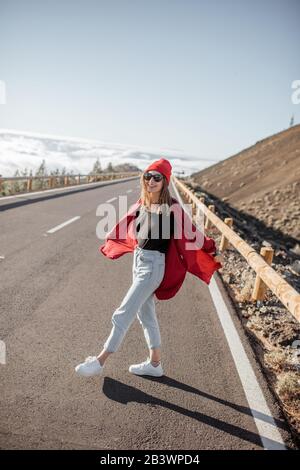 Portrait d'une femme gaie vêtue de rouge chemise et chapeau, se sentant libre et joyeuse sur la route au-dessus des nuages. Style de vie et concept de voyage insouciant Banque D'Images