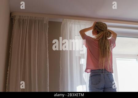 Femme accrochant des rideaux à la fenêtre Banque D'Images