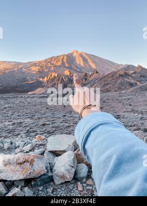 Femme pointant à la main sur la montagne volcanique pendant un coucher de soleil, gros plan sur la main. Image réalisée sur le téléphone portable Banque D'Images