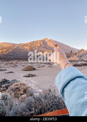 Femme pointant à la main sur la montagne volcanique pendant un coucher de soleil, gros plan sur la main. Image réalisée sur le téléphone portable Banque D'Images