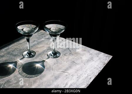 Gobelets en verre avec cocktail sur fond argent. Reflet et reflet du soleil. Fond noir minimal Banque D'Images