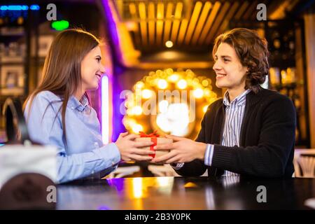 Homme romantique donnant cadeau d'anniversaire à une belle femme émotionnelle. Portrait de couple assis ensemble dans le café, datant. Concept de Saint Valentin Banque D'Images