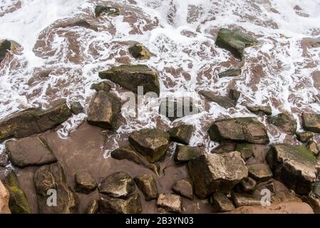 Eau de mer brouillée, avec mousse blanche, entre les rochers de la rive. Vue de dessus. Banque D'Images