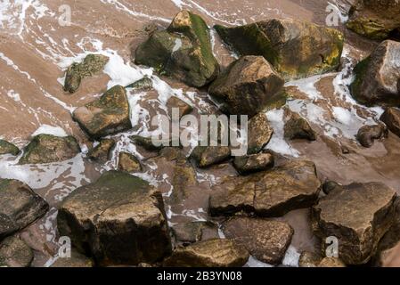 Eau de mer brouillée, avec mousse blanche, entre les rochers de la rive. Vue de dessus. Banque D'Images