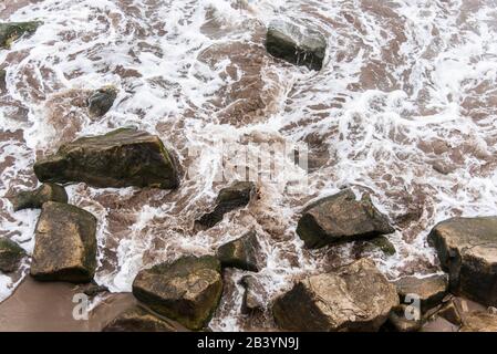 Déplacer l'eau de mer, avec de la mousse blanche, entre les roches du rivage. Vue de dessus. Banque D'Images