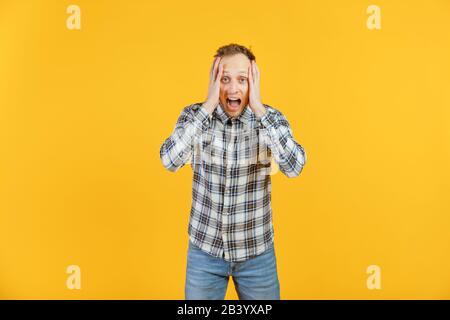 Portrait de choqué stupéfait surpris jeune homme avec la bouche large ouverte, les mains sur la tête hurlant criant criant, isolé sur fond jaune Banque D'Images