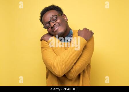Heureux l'homme africain américain dans les vêtements et les verres jaunes se hople lui-même, a une haute estime de soi. Studio tourné sur un mur coloré. Banque D'Images