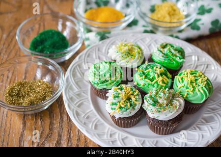 Une plaque de mini-cupcakes au chocolat givré vert et blanc décorés de saupoules assorties or, jaune et vert. Les saupoules sont floues dans le dos Banque D'Images