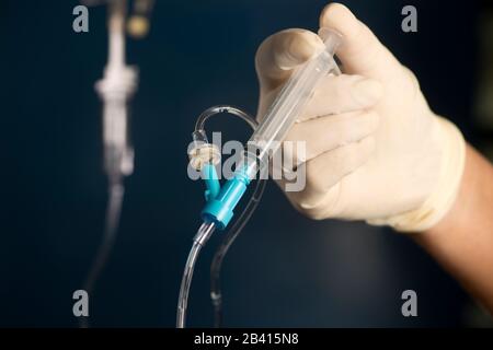 L'infirmière pousse le médicament IV par seringue dans le port IV avec un fond bleu. Banque D'Images