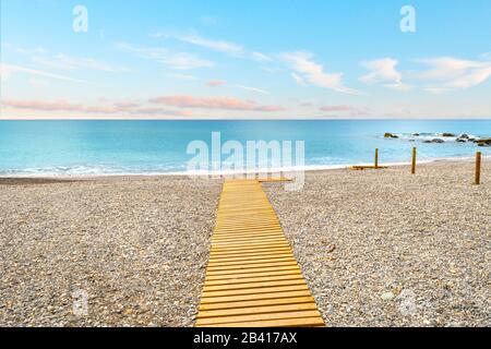 Une scène de plage avec de l'eau bleu d'aqua colorée et le ciel au-dessus d'une passerelle en bois sur la côte de Ventimiglia, Italie. Banque D'Images