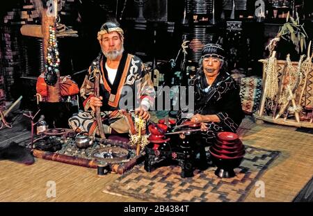 Un couple âgé d'Ainu pose en robe traditionnelle avec des souvenirs qu'ils vendent dans une maison natale qui est ouverte aux touristes sur l'île d'Hokkaido dans le nord du Japon. L'homme barbu de 70 ans est assis à côté de sa tante de 84 ans avec un tatouage autour de sa bouche qui ressemble à une moustache. La douloureuse tradition de la suie à frotter dans les coupes dans la peau pendant l'enfance pour combattre les mauvais esprits et pour indiquer qu'une fille était prête pour le mariage a depuis été proscrit par le gouvernement japonais. La femme était l'une des 300 Ainu pur-blooded vivant encore quand cette photographie historique a été prise en 1962. Banque D'Images