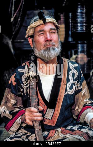 Un homme de 70 ans barbu Ainu vêtu d'une robe traditionnelle et portant une couronne de fibres de bois possède une épée cérémonielle dans une maison natale sur l'île d'Hokkaido dans le nord du Japon. Ses vêtements ont des motifs pour se défaire des mauvais esprits. L'homme était l'un des 300 Ainu pur-blooded (prononcé I-noo) encore vivant quand il a posé pour cette photographie historique en 1962. Depuis cette époque, les Ainu s'assimilent à la société japonaise et à leurs vieux métiers d'art, les coutumes et les cérémonies ne sont maintenues en vie que dans des villages spéciaux pour les touristes. L'Ainu a été officiellement reconnu comme peuple autochtone du Japon en 2008. Banque D'Images