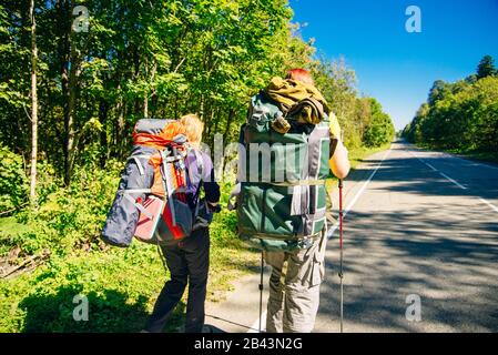 Un jeune touriste avec un grand sac à dos marche sur une route d'asphalte Banque D'Images