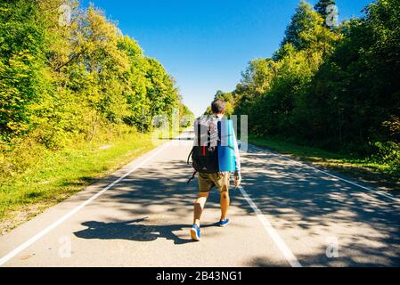 Un jeune touriste avec un grand sac à dos marche sur une route d'asphalte Banque D'Images