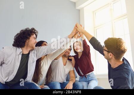 Les amis heureux ont gentièrement levé les mains dans une chambre avec une fenêtre. Banque D'Images