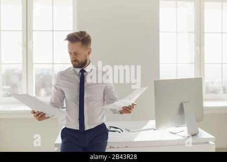 Homme d'affaires blond avec des documents en mains debout travaillant au bureau Banque D'Images
