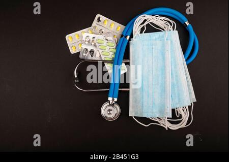 Masque médical jetable, stéthoscope et quelques paquets de pilules sur fond noir. Protection individuelle contre les maladies infectieuses. Fermer u Banque D'Images