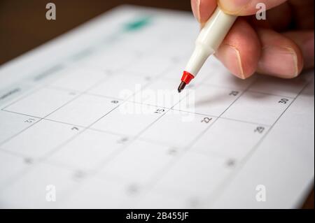 La main d'un homme tenant un stylo dans sa main et enregistrant son programme sur un calendrier de bureau Banque D'Images