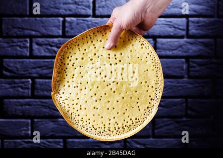 La main de femme tient des manis de martabak pancake épais indonésiens devant le mur de briques noires Banque D'Images