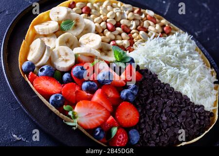 Cuisine traditionnelle asiatique de rue: Pancake de lune brillant ou martabak avec des copeaux de chocolat, des arachides, des fraises, des bleuets, des bananes, du fromage, sur du béton b Banque D'Images