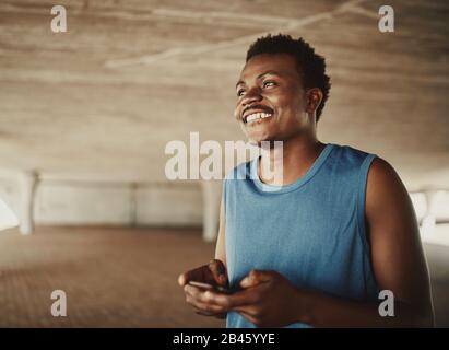 Installez le jeune homme africain américain en souriant avec un smartphone et en regardant à l'extérieur Banque D'Images