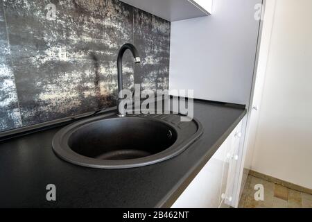 Intérieur d'une cuisine moderne et spacieuse avec mobilier contemporain blanc, carrelage en céramique noire sur le mur et évier en granit sombre avec robinet d'eau. Banque D'Images