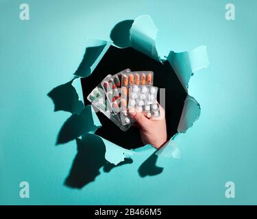 Assortiment de pilules ou de capsules avec des médicaments à la main encadrés par un trou de papier. Fond de trou de papier déchiré à la mode bleu menthe. Sélection de médicaments, su alimentaire Banque D'Images