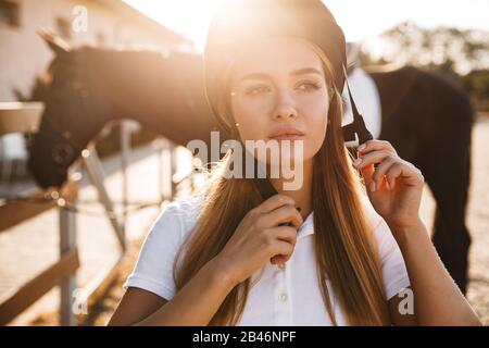 Photo de belle concentré sérieuse jeune blonde belle femme portant chapeau avec cheval dans la campagne en plein air Banque D'Images