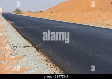 Nouvelle route asphaltée dans le sable du désert sans voiture ni personne. Construction, désolate, chaud, aride concepts. Banque D'Images