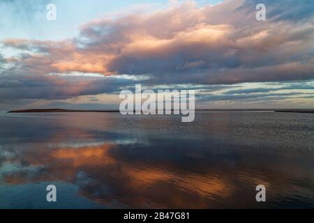 La lumière orange d'un coucher de soleil d'hiver se reflétant dans les eaux peu profondes et calmes autour des rives de sable de St Cyrus Beach dans Aberdeenshire. Banque D'Images