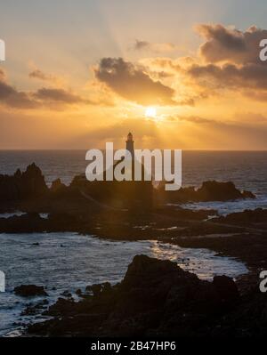 Phare de Corbiere avec poutres apparentes en streaming dans les nuages. Jersey, îles Anglo-Normandes Banque D'Images